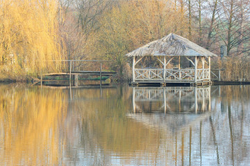 Fototapeta na wymiar Wooden arbour in autumn by a lake with reflections