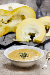 Pumpkin soup on rustic wooden table. Raw pumpkins in the backgro