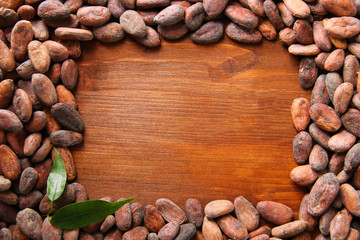 Cocoa beans with leaves on wooden background
