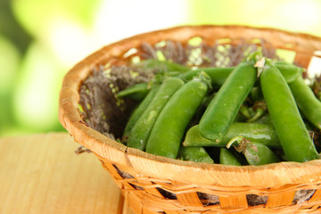 Green peas in basket on wooden table on nature background