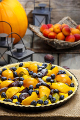 Tart with peach, pumpkin, plum and blueberry in autumn setting