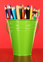 Color bucket with multicolor pencils, on color background