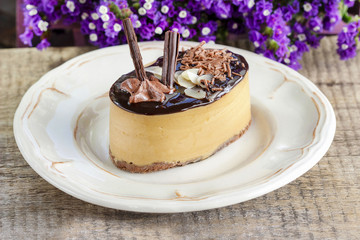 Cappuccino cake on white plate. Purple flowers in the background