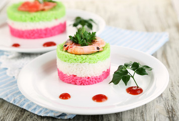Colored rice on plates on napkin on wooden table