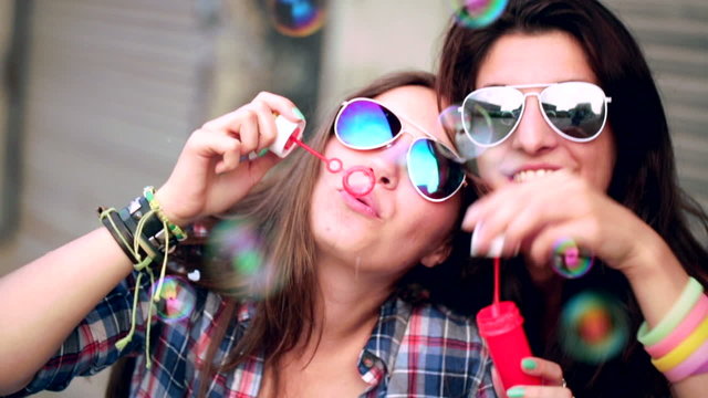 Teenage hipster friends cheerfully making soap bubbles