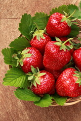 Basket od fresh strawberries with leaves on wooden  background