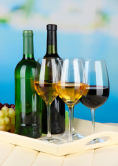 Wine bottles and glasses of wine on tray, on bright background