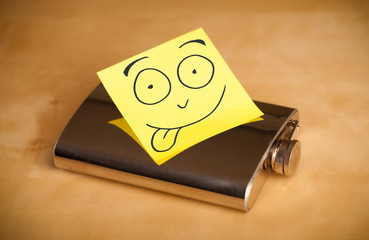 Post-it note with smiley face sticked on a hip flask