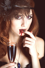 Redhead vampire woman with glass of blood. Photo in vintage styl