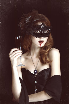 Redhead vampire woman in mask with glass of blood.
