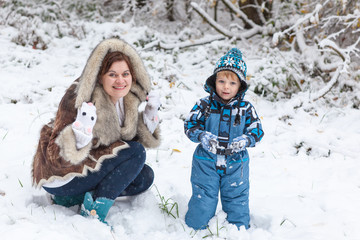 Fototapeta na wymiar Mother and toddler boy having fun with snow on winter day