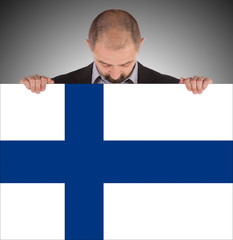 Smiling businessman holding a big card, flag of Finland - obrazy, fototapety, plakaty