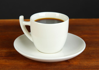 Cup of coffee on wooden table on black background