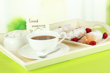 Cup of tea with cakes on wooden tray on table in room
