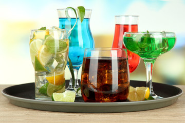 Many glasses of cocktails on tray on table, on bright