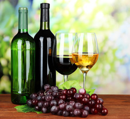 Wine bottles and glasses of wine on bright background