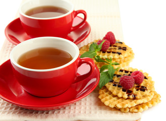 Cups of tea with cookies and raspberries isolated on white