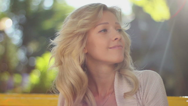 Young blond female enjoys life in sunlight, combing hair smiling