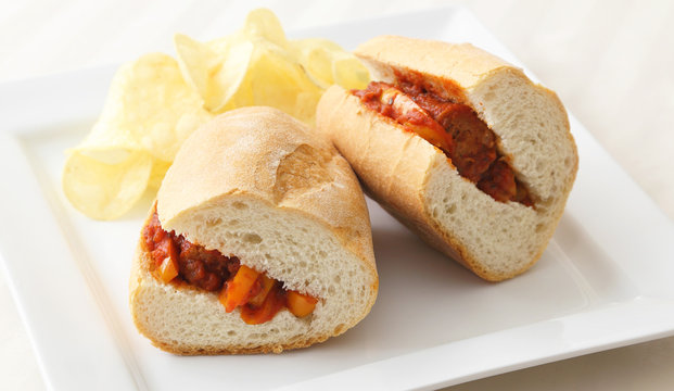 Sausage and peppers sandwich served with a side of potato chips