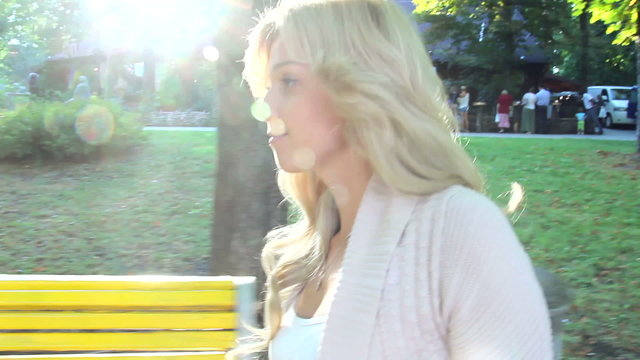 Following beautiful blond woman turns and smiles to camera park