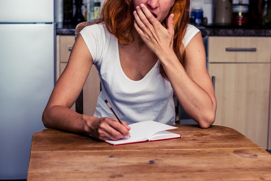 Tired woman writing in her kitchen
