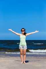 Teenage girl standing on beach, arms up