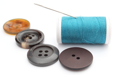 Sewing buttons and spool of thread on white background