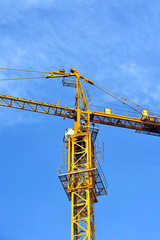Yellow construction tower crane against blue sky