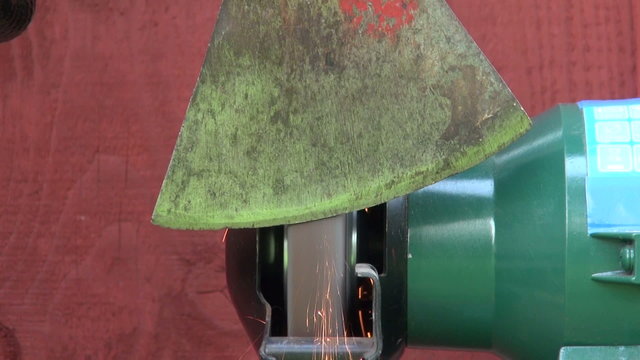 sharpening old axe tool on electrical grinder stone