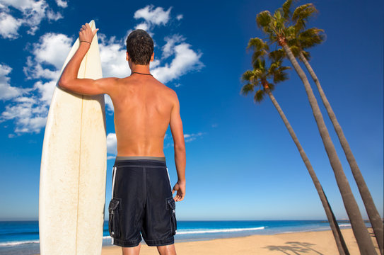 Boy surfer back view holding surfboard on beach