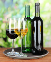 Wine bottles and glasses of wine on tray, on bright background