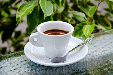 White espresso cup standing on the glass table of street cafe
