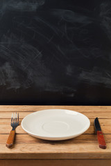 Empty plate on wooden table over chalkboard background