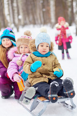 Older girl pushes sled with two little children, first asian boy