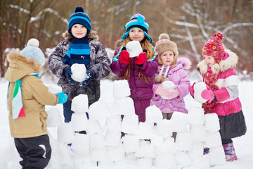 Five children build wall from snow bricks in winter park