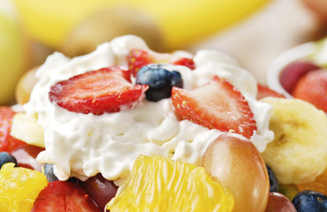 Sweet tasty fruit salad in the bowl with whipped cream