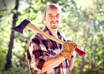 portrait of a smiling caucasian woodcutter with his ax. natural and bright background.