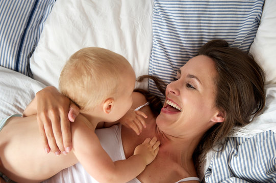 Portrait of a happy mother playing with baby in bed