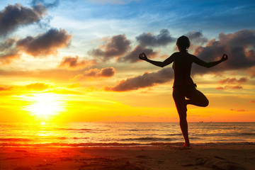 Fototapeta na wymiar Young woman practicing yoga on the beach at sunset