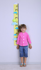 Little girl measuring height against wall in room