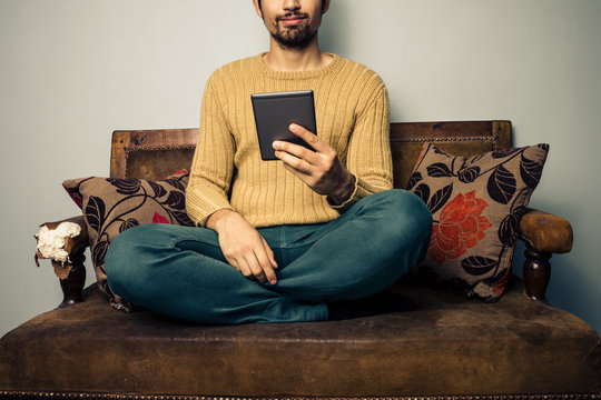 Young man sitting on sofa reading on tablet