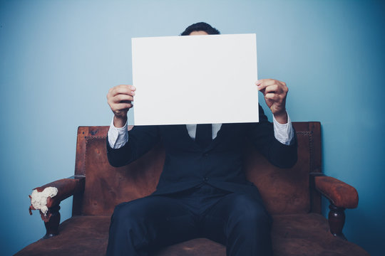 Businessman sitting on sofa holding blank white sign