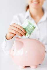 woman puts euro cash into large piggy bank