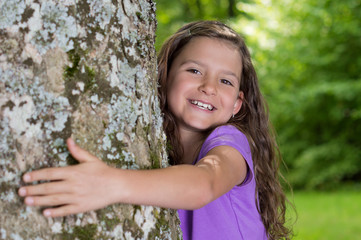 Kleines Mädchen umarmt Freudestrahlend einen Baum