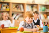 Little redhead schoolboy behind school desk