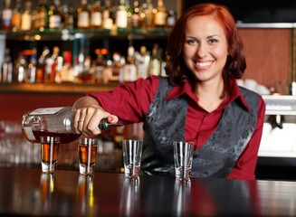 Beautiful redhead barmaid making shots