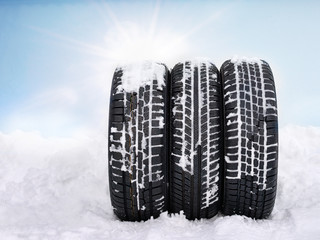 Three snowy winter tyres in front of blue sky with sunlights