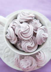 Meringues in a white teacup on a lilac color background
