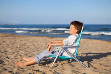 Thoughtful boy sitting on chair at beach