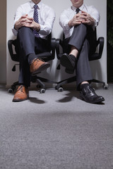 Fototapeta na wymiar Two businessmen sitting down with legs crossed, low section